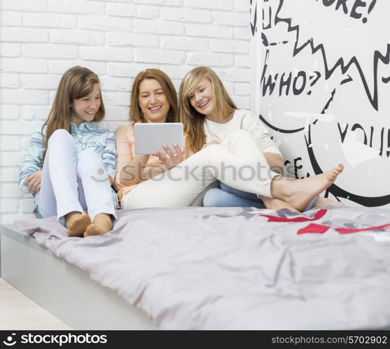 Mother with daughters using digital tablet in bedroom