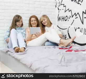 Mother with daughters using digital tablet in bedroom