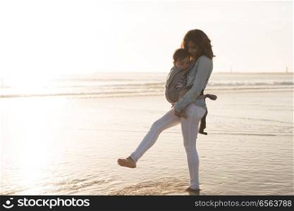 Mother with ergobaby carrying toddler on the beach