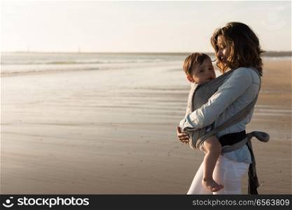 Mother with ergobaby carrying toddler on the beach