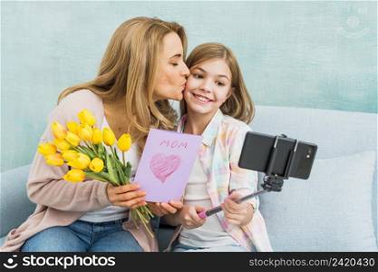 mother with gifts kissing daughter taking selfie