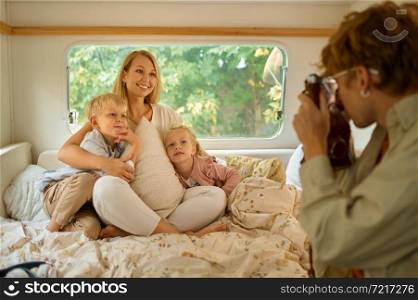 Mother with her children poses in motorhome, summer camping. Couple with kids travel in camp car, trailer interior on background. Campsite adventure, travelling lifestyle, vacation on rv vehicle. Mother with children poses in motorhome, camping