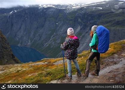mother with her daughter hikers are standing on a path and looking at the fjord