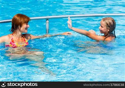Mother with her daughter in the summer outdoor pool.