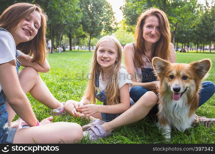 mother with her daughters and dog are sitting on a grass at the park