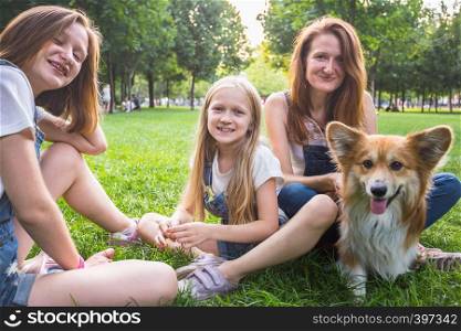 mother with her daughters and dog are sitting on a grass at the park