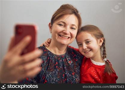 Mother with her little daughter making video call using mobile phone. Keeping distance. Woman and little girl talking with relatives. Cheerful family having fun taking selfie photo using smartphone. Connecting remotely with family