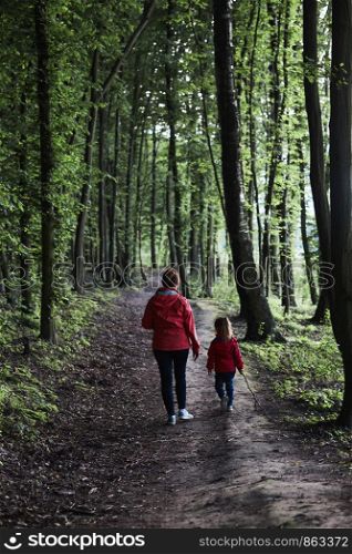 Mother with her little daughter walking through the forest. Spending leisure time, vacation on wandering in forests, close to nature
