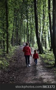 Mother with her little daughter walking through the forest. Spending leisure time, vacation on wandering in forests, close to nature