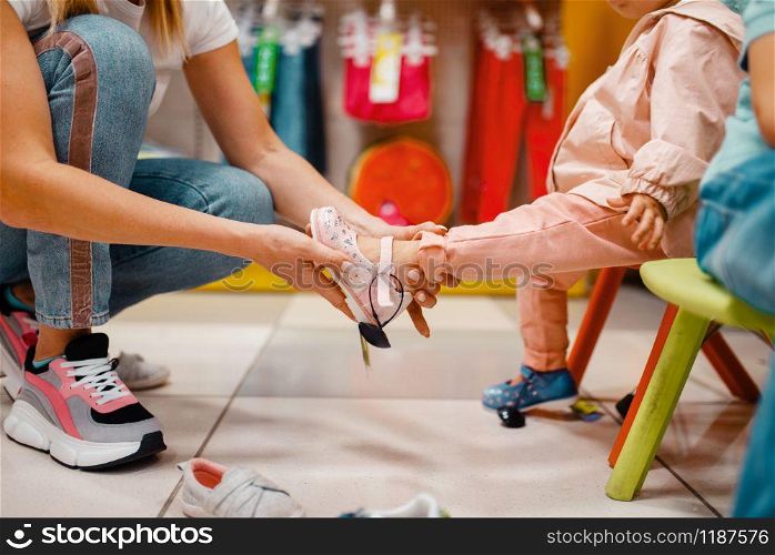 Mother with her little girl choosing shoes in kids store. Mom and child buying clothes in supermarket together, family shopping