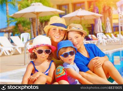 Mother with kids relaxing on beach resort, sitting near poolside, active summer holidays, young tourists, happy family concept