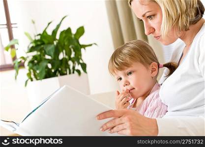 Mother with little girl read book together in lounge