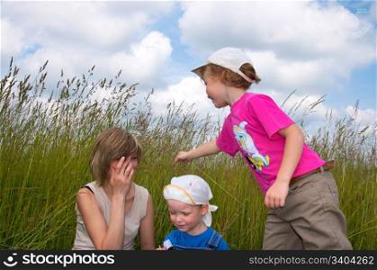 Mother with small children play in tallgrass on meadow