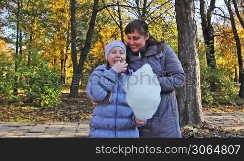 mother with teen daughter standing eat cotton candy in beautiful autumn city park