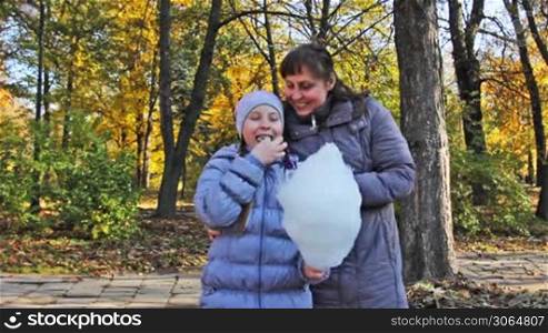 mother with teen daughter standing eat cotton candy in beautiful autumn city park