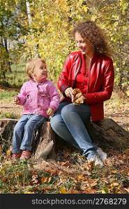 mother with the daughter sits in the park in autumn