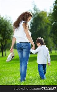 Mother with the small son barefoot walk on a summer grass in park