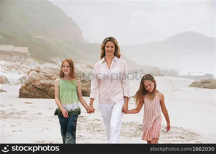 Mother with two daughters (7-9 10-12) walking on beach