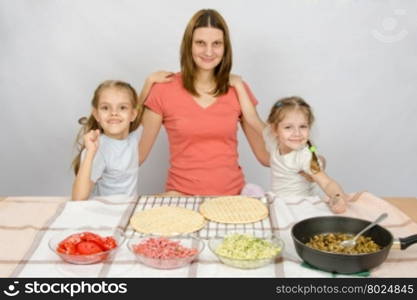 Mother with two daughters at the kitchen table are going to cook a pizza and a fun look into the frame