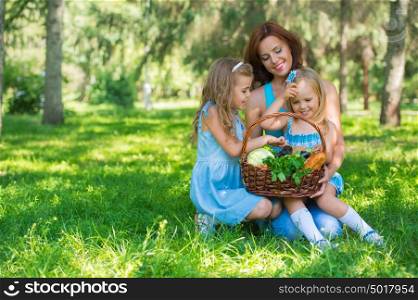 Mother with two daughters in the park preparing for picnic of organic food