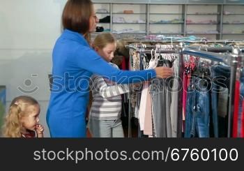 Mother with two daughters shopping for clothes in a clothing store, looking tunic sweater, denim skirt
