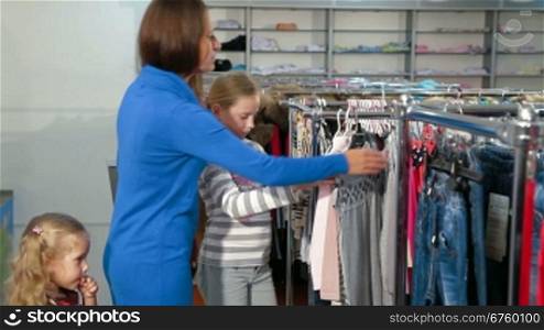 Mother with two daughters shopping for clothes in a clothing store, looking tunic sweater, denim skirt