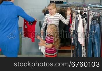 Mother with two daughters shopping for girls clothes in a clothing store, looking skirt and sweater