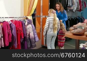 Mother with two daughters shopping for girls clothes in a clothing store, child trying on dress