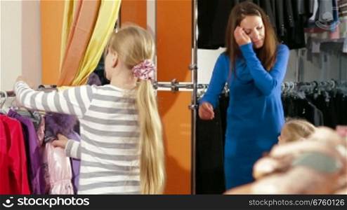Mother with two daughters shopping for girls clothes in a clothing store, child trying on warmest jacket