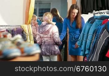 Mother with two daughters shopping for girls clothes in a clothing store, child trying on warmest jacket