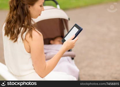 motherhood, leisure and technology concept - close up of mother with child in stroller reading internet book at summer park. mother with stroller reading internet book at park