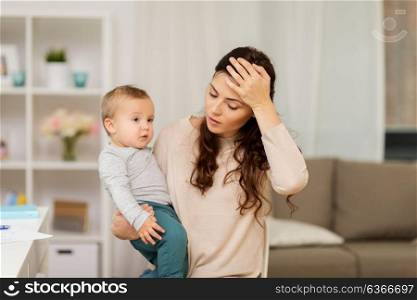 motherhood, multi-tasking and family concept - tired mother having headache with baby boy at home. tired mother with baby boy at home
