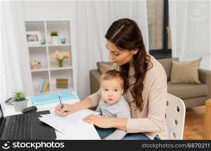 motherhood, multi-tasking, family and people concept - happy mother with baby, papers and laptop working at home. happy mother with baby and papers working at home. happy mother with baby and papers working at home