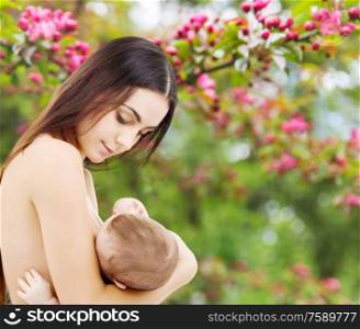 motherhood, nutrition and people concept - mother breastfeeding her baby over natural spring cherry blossom background. mother breastfeeding her baby over garden