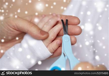 motherhood, people and child care concept - close up of mother hand with scissors trimming baby nails over snow. close up of hand with scissors trimming baby nails
