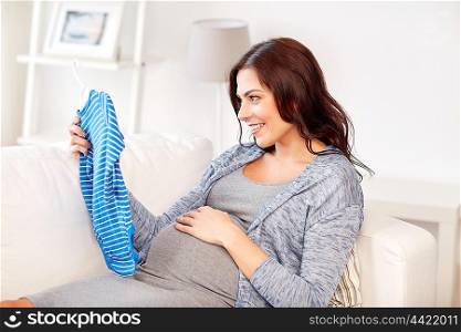 motherhood, pregnancy, people and kids clothing concept - happy woman holding and looking at blue baby boys bodysuit at home