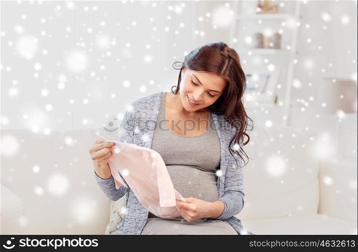 motherhood, pregnancy, people and kids clothing concept - happy woman holding and looking at pink baby girls bodysuit at home over snow