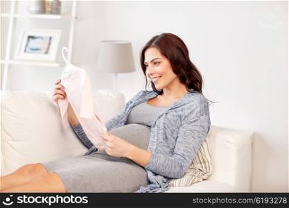 motherhood, pregnancy, people and kids clothing concept - happy woman holding and looking at pink baby girls bodysuit at home
