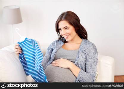 motherhood, pregnancy, people and kids clothing concept - happy woman holding and looking at blue baby boys bodysuit at home