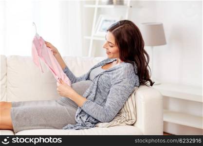 motherhood, pregnancy, people and kids clothing concept - happy woman holding and looking at pink baby girls bodysuit at home