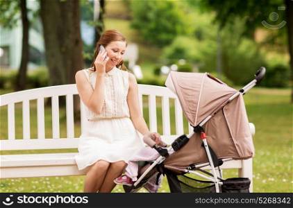 motherhood, technology and people concept - happy mother with baby girl in stroller calling on smartphone at summer park. happy mother with smartphone and stroller at park