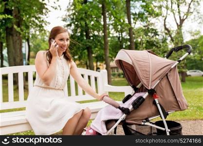 motherhood, technology and people concept - happy mother with baby girl in stroller calling on smartphone at summer park. mother with stroller calling on smartphone at park