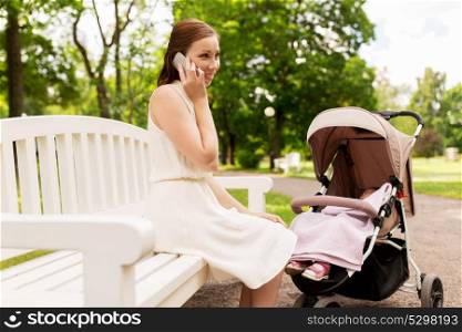 motherhood, technology and people concept - happy mother with baby girl in stroller calling on smartphone at summer park. mother with stroller calling on smartphone at park