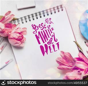 Mothers Day Greeting card with text lettering in german Beste Mutter der Welt , pale pink tulips, notebook or sketchbook and colorful brush markers , top view
