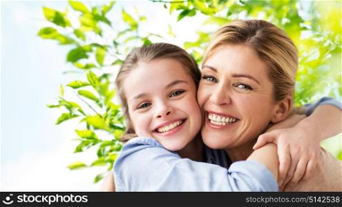 mothers day, people and family concept - happy smiling girl with mother hugging over green natural background. happy family of girl and mother hugging
