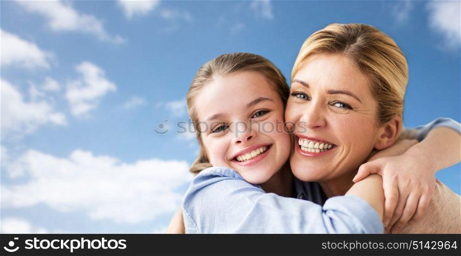 mothers day, people and family concept - happy smiling girl with mother hugging over blue sky and clouds background. happy family of girl and mother hugging over sky