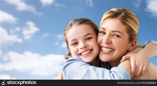 mothers day, people and family concept - happy smiling girl with mother hugging over blue sky and clouds background. happy family of girl and mother hugging over sky