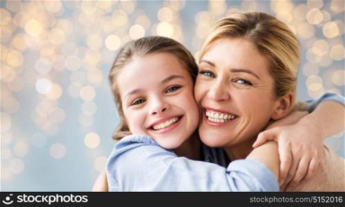 mothers day, people and family concept - happy smiling girl with mother hugging over lights background. happy family of girl and mother hugging