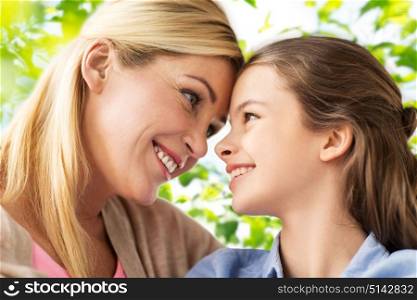 mothers day, people and family concept - happy smiling girl with mother over green natural background. happy family of girl and mother