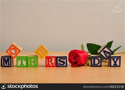 Mothers day spelled with colorful alphabet blocks and a red rose